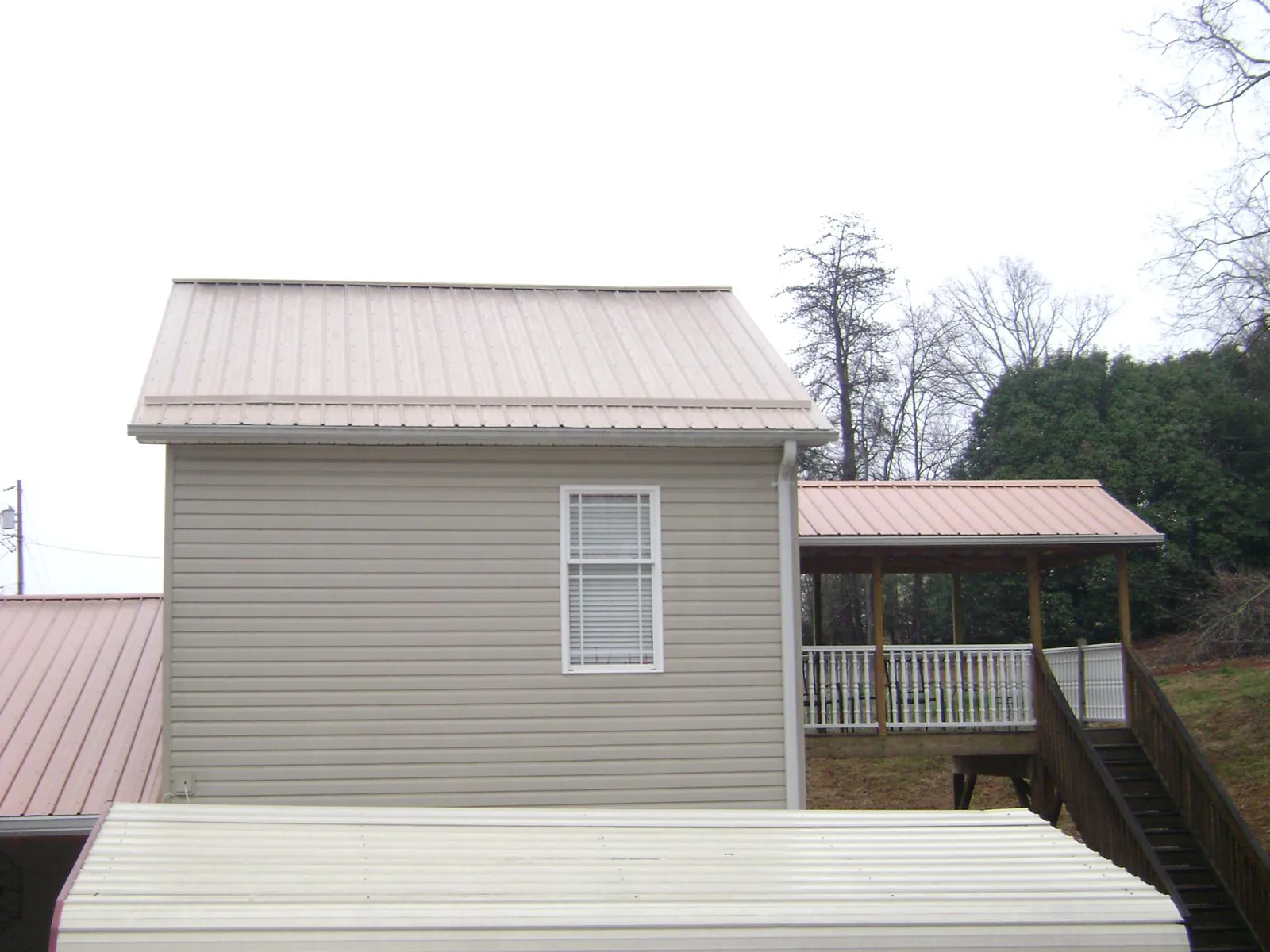 Tan metal roofs on a two story addition and attached porch, from a Roof Replacement job in Franklin
